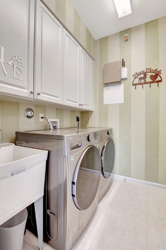 laundry area with light tile patterned floors, separate washer and dryer, a sink, baseboards, and cabinet space