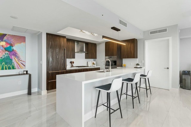 kitchen with a breakfast bar area, wall chimney range hood, modern cabinets, and visible vents