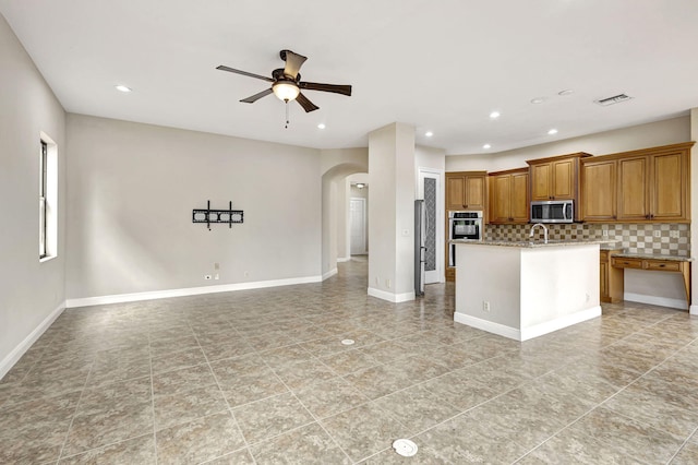 kitchen featuring a center island with sink, tasteful backsplash, stainless steel appliances, ceiling fan, and sink