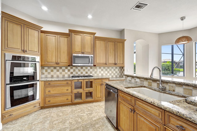 kitchen with stainless steel appliances, light stone counters, pendant lighting, backsplash, and sink