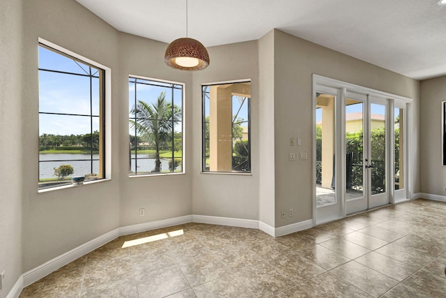 empty room with a water view, french doors, light tile patterned floors, and a healthy amount of sunlight