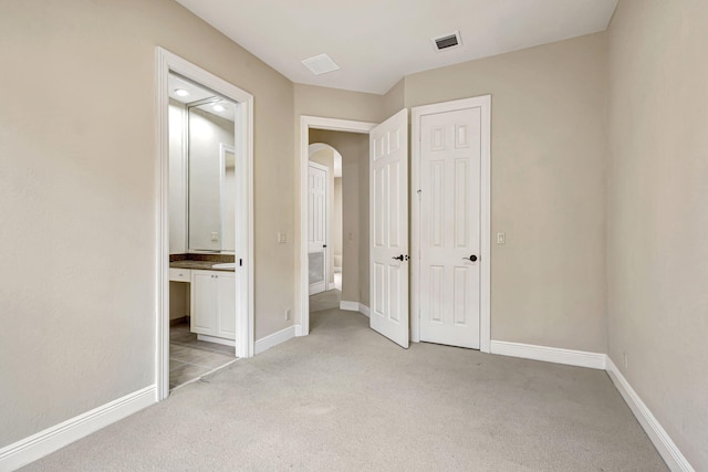 unfurnished bedroom featuring light carpet and ensuite bathroom