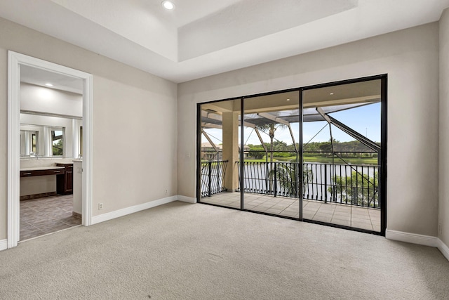 spare room featuring a water view, a tray ceiling, and light colored carpet