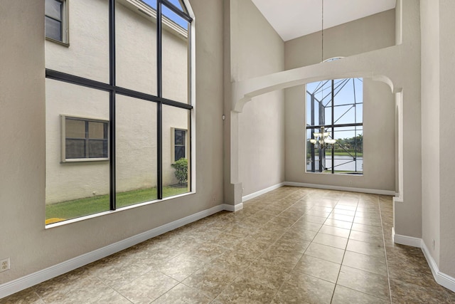 empty room featuring a towering ceiling, an inviting chandelier, and light tile patterned floors