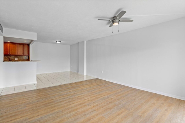 unfurnished living room featuring a ceiling fan, light wood-type flooring, and baseboards