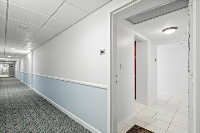 corridor featuring light carpet, light tile patterned floors, baseboards, visible vents, and a paneled ceiling