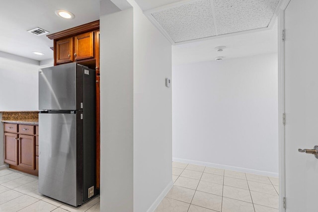 kitchen with light tile patterned flooring, visible vents, baseboards, freestanding refrigerator, and brown cabinets