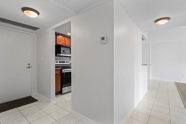 hallway featuring a textured ceiling, light tile patterned flooring, and baseboards