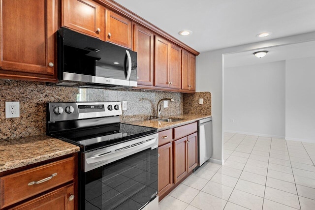 kitchen with light tile patterned floors, appliances with stainless steel finishes, brown cabinets, light stone counters, and a sink