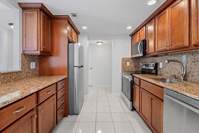 kitchen with light stone counters, visible vents, appliances with stainless steel finishes, brown cabinetry, and a sink