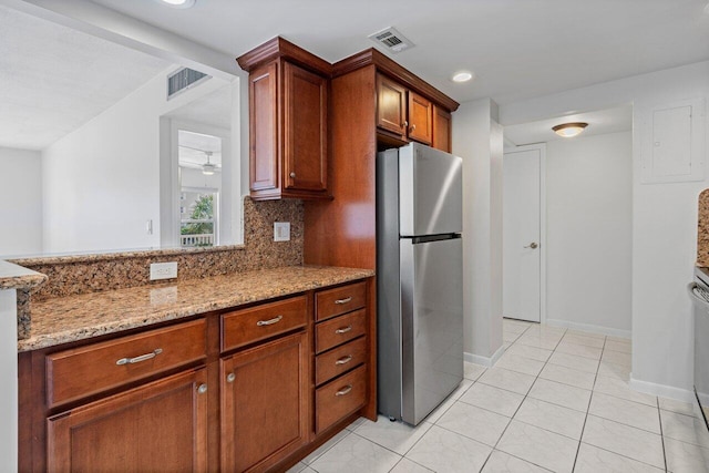 kitchen featuring visible vents, light stone counters, freestanding refrigerator, and tasteful backsplash