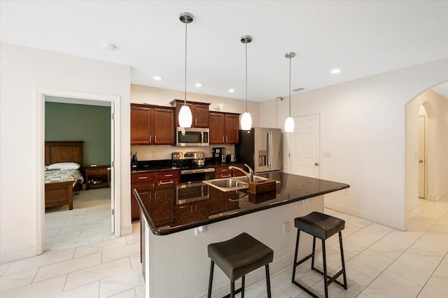 kitchen with arched walkways, appliances with stainless steel finishes, a kitchen island with sink, a kitchen bar, and a sink