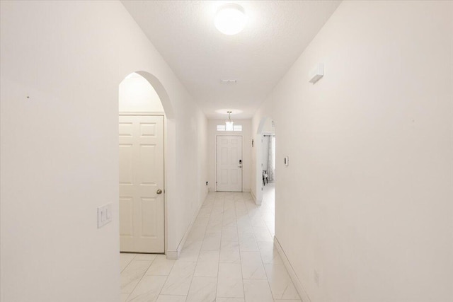 corridor with arched walkways, a textured ceiling, and baseboards