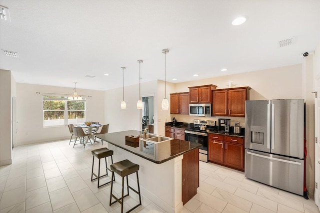 kitchen with stainless steel appliances, dark countertops, a sink, an island with sink, and a kitchen bar