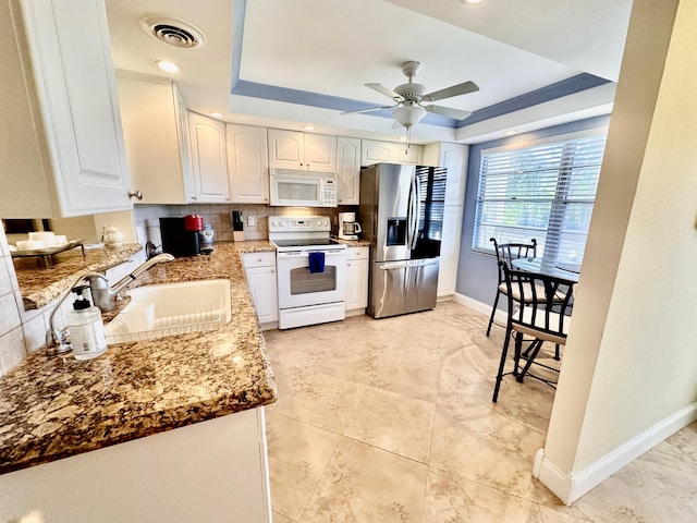 kitchen with a tray ceiling, white appliances, visible vents, and white cabinets