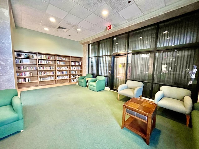 sitting room featuring carpet floors, wall of books, and visible vents