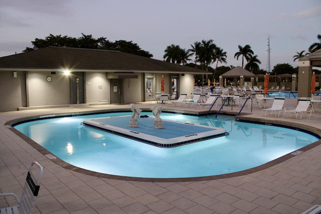 pool at dusk with a patio and a community pool