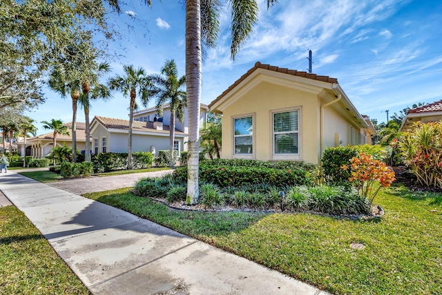 view of side of home featuring stucco siding, a lawn, and a tile roof