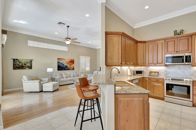 kitchen featuring appliances with stainless steel finishes, a breakfast bar, open floor plan, a sink, and a peninsula