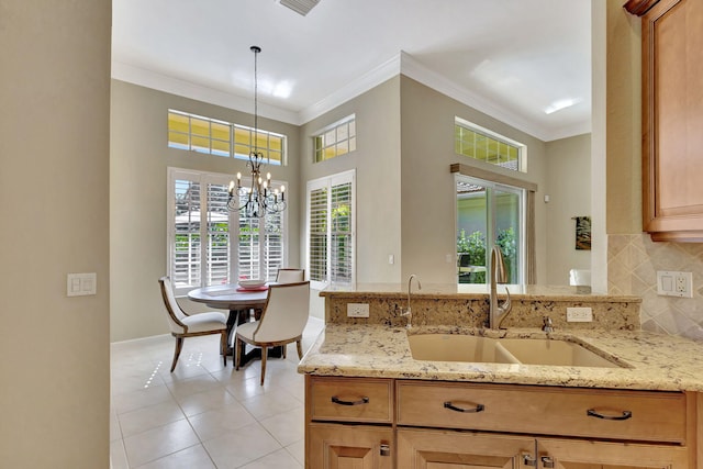 kitchen with ornamental molding, decorative backsplash, light stone counters, a sink, and decorative light fixtures