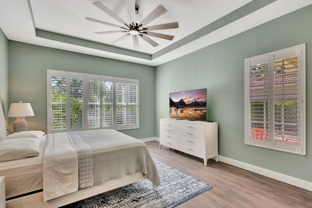 bedroom featuring baseboards, ceiling fan, wood finished floors, and a tray ceiling