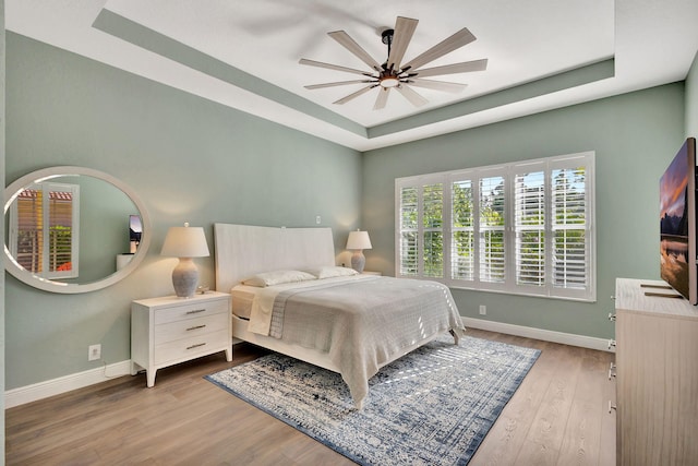 bedroom with baseboards, ceiling fan, light wood finished floors, and a tray ceiling