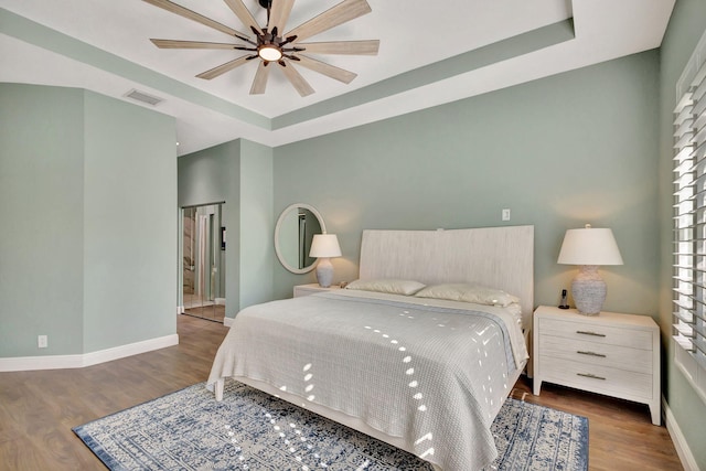 bedroom featuring dark wood-style floors, a ceiling fan, baseboards, visible vents, and a tray ceiling