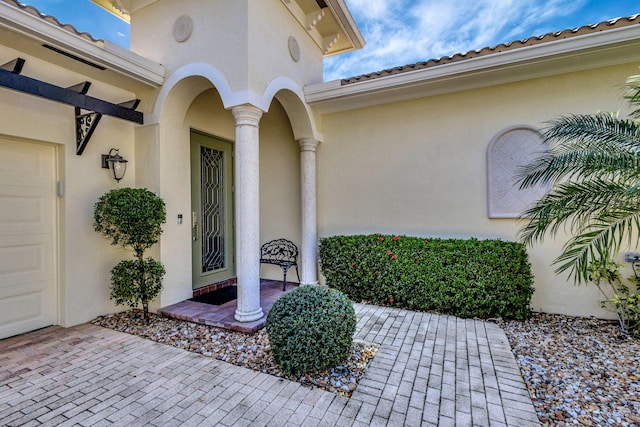 property entrance with stucco siding, an attached garage, and a tile roof