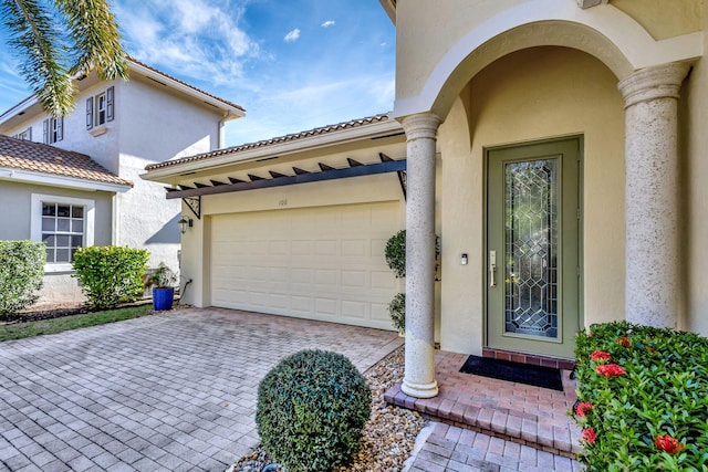 doorway to property featuring stucco siding, decorative driveway, and a garage