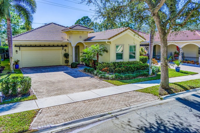 mediterranean / spanish-style home featuring stucco siding, a tiled roof, decorative driveway, and a garage