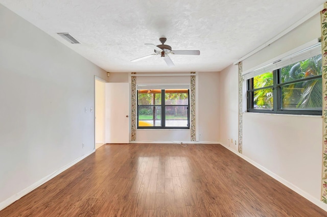 empty room with visible vents, ceiling fan, a textured ceiling, wood finished floors, and baseboards