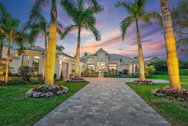 prairie-style home with a garage, decorative driveway, french doors, a front lawn, and stucco siding