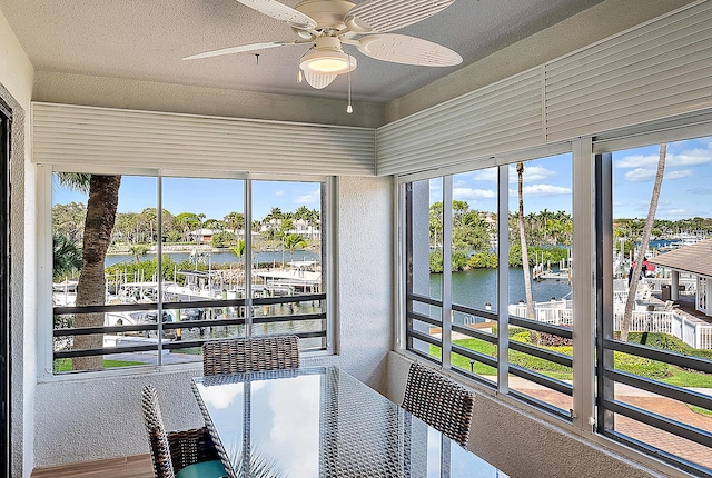 sunroom featuring a healthy amount of sunlight, ceiling fan, and a water view