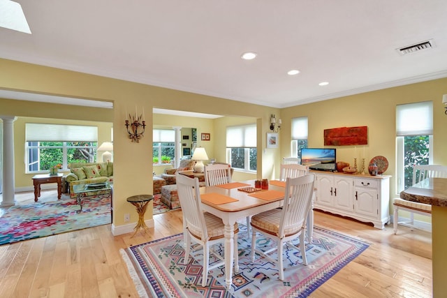 dining room featuring visible vents, light wood-style floors, a healthy amount of sunlight, and ornate columns