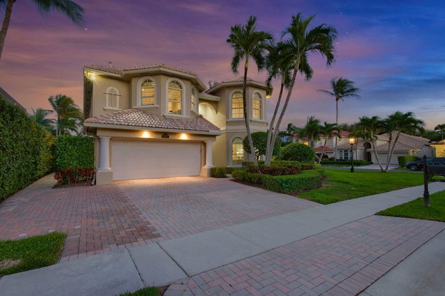 mediterranean / spanish home featuring a tile roof, an attached garage, decorative driveway, a yard, and stucco siding