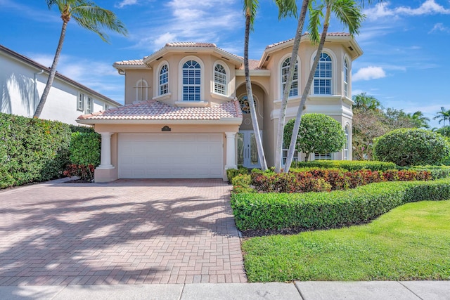 mediterranean / spanish house featuring a garage, decorative driveway, a tiled roof, and stucco siding