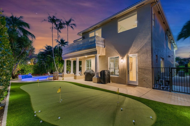 back of house at dusk with a patio area, fence, a balcony, and stucco siding