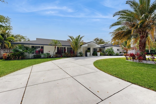 view of front of home with concrete driveway, fence, a front yard, and stucco siding