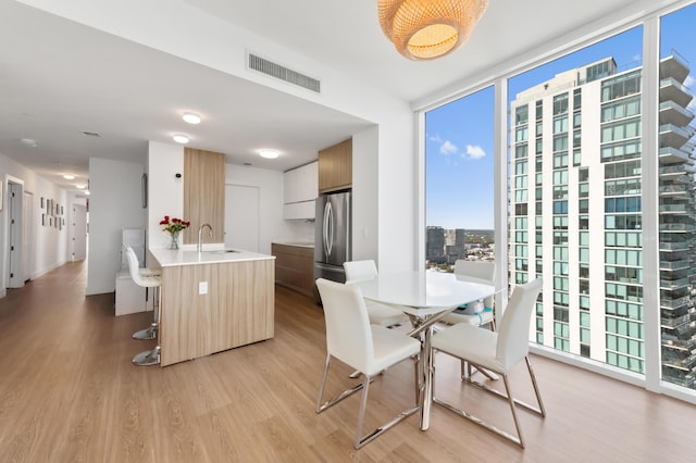 dining room featuring light wood-style flooring, expansive windows, a city view, and visible vents