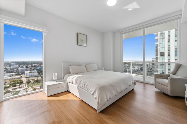 bedroom with access to exterior, light wood-style floors, a wall of windows, and a city view