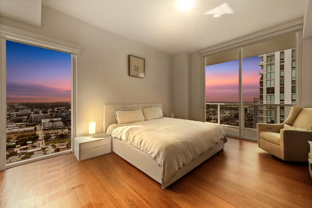 bedroom with a view of city, access to outside, expansive windows, and wood finished floors