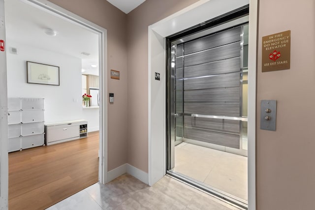 doorway featuring baseboards, light wood-type flooring, and elevator