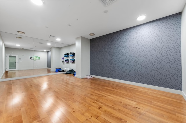 exercise room featuring wallpapered walls, visible vents, baseboards, light wood-style flooring, and an accent wall