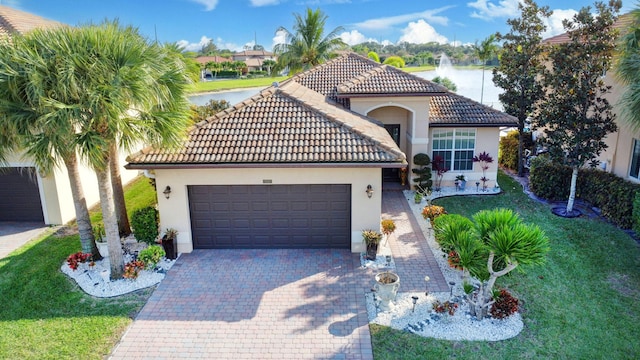 mediterranean / spanish house featuring a garage, decorative driveway, a water view, and stucco siding