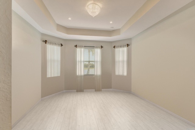 spare room with light wood finished floors, baseboards, a raised ceiling, and recessed lighting