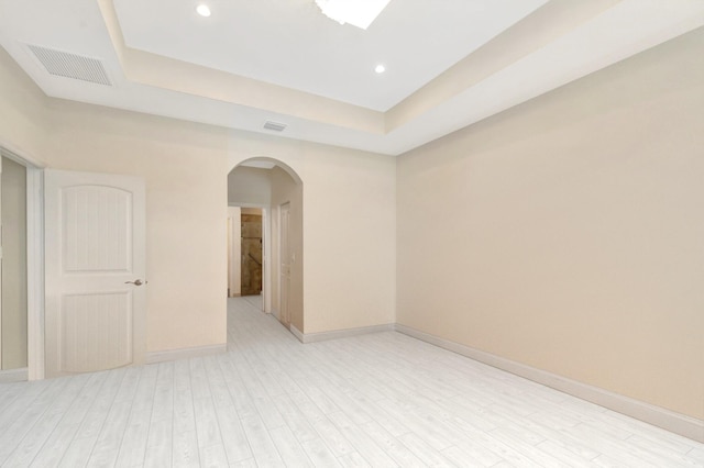 spare room featuring arched walkways, a raised ceiling, visible vents, light wood-style flooring, and baseboards