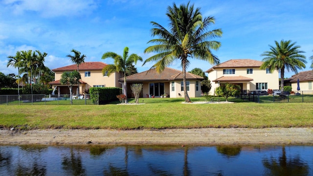 rear view of property featuring a lawn, a water view, fence, and stucco siding