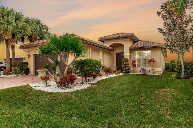 mediterranean / spanish home featuring decorative driveway, a lawn, a tiled roof, and stucco siding