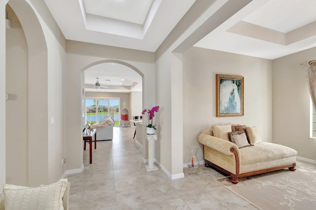 hallway featuring baseboards, a tray ceiling, and arched walkways