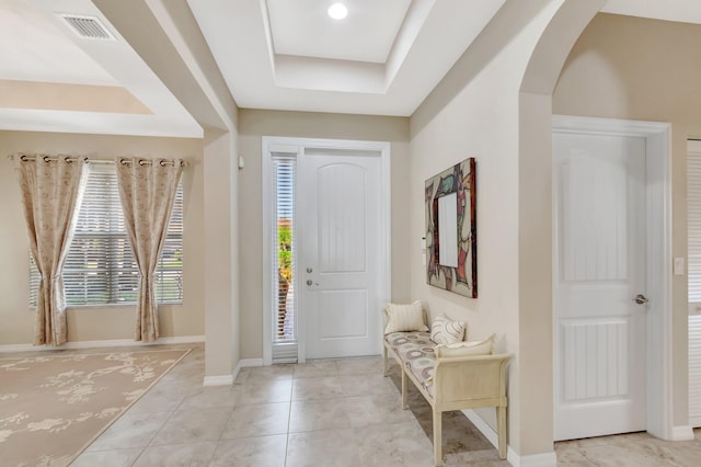 tiled entrance foyer with arched walkways, a tray ceiling, visible vents, and baseboards